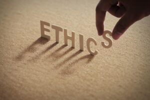 ETHICS wood word on compressed board with human's finger at S letter