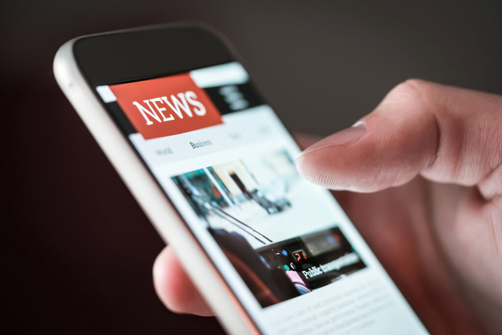 Mobile phone being held by the hand of a while male, with "news" written on the phone.