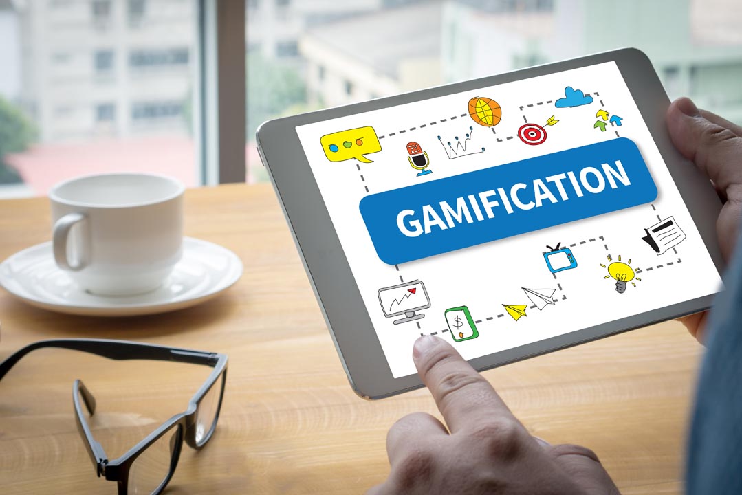 Tablet device being held in an office showing the word "gamification" and various playing icons on the screen.