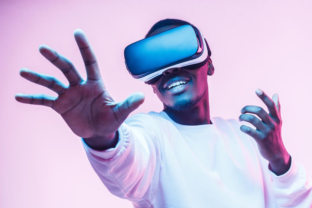 A man of colour, wearing a virtual reality headset, reaching out towards the camera.