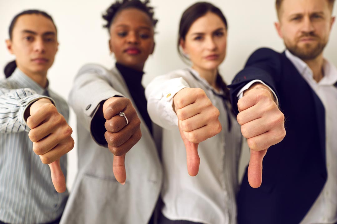 Group of disappointed young multiethnic people give thumbs down, hands in closeup.