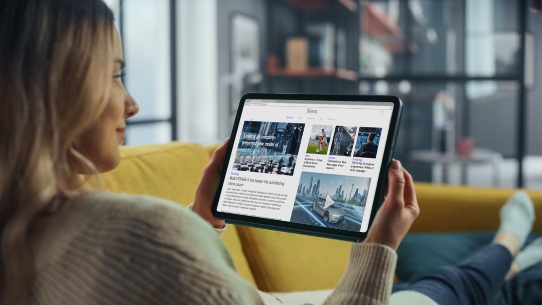Woman on a sofa holding a tablet looking at content.
