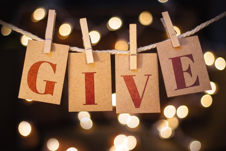 The word "give" in letters on card pegged up with lights in the background