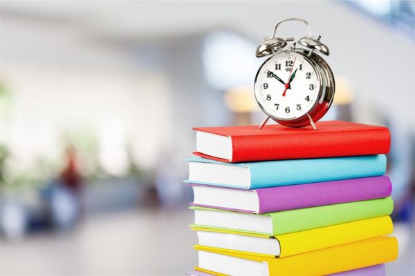 Pile of colourful books and alarm clock on top on white background