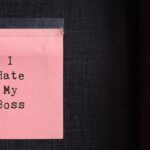 Pink sticky note with text typed I HATE MY BOSS on the office wall