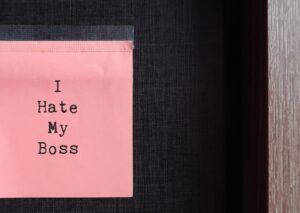 Pink sticky note with text typed I HATE MY BOSS on the office wall