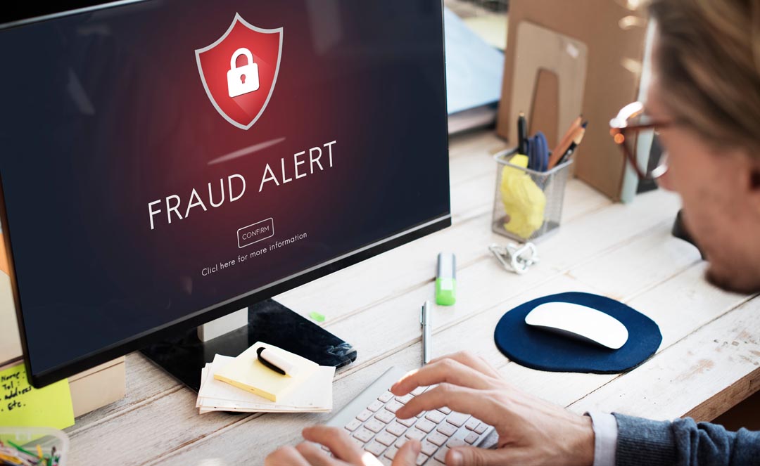 Fraud Alert Caution on a computer screen with a person sitting at an office desk.