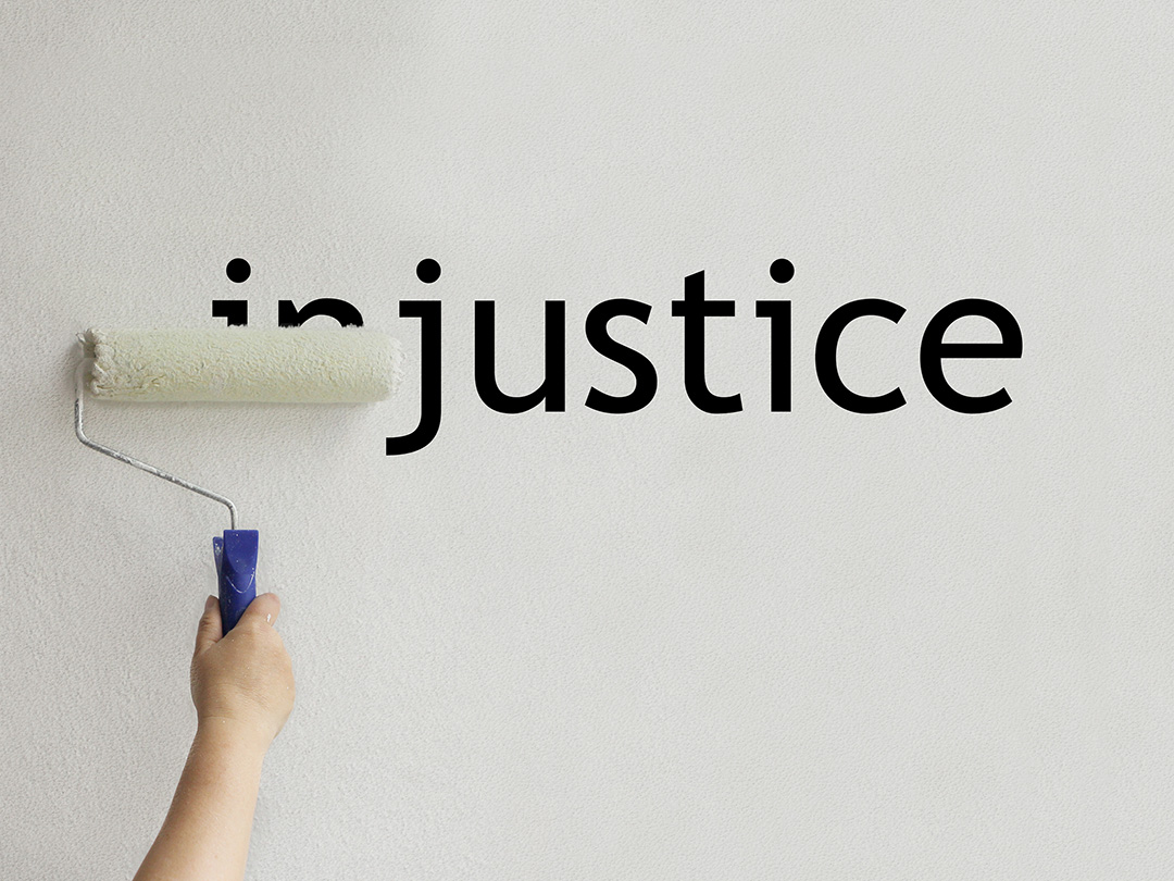 The word injustice on a wall and the first two letters being painted over with a roller