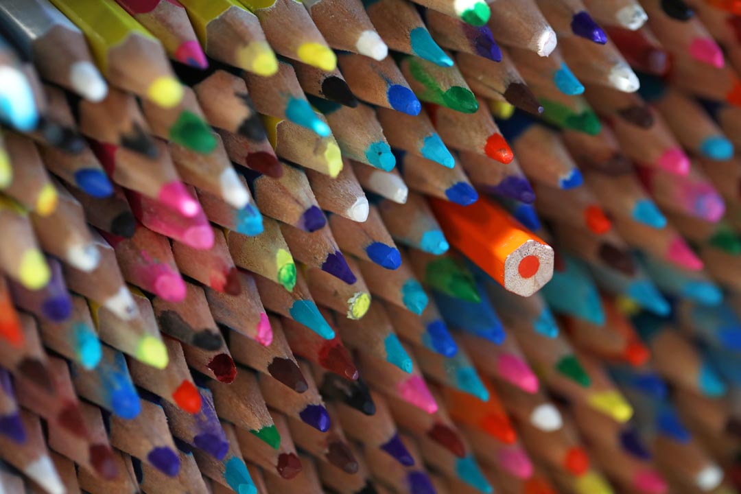 A large stack of masses of sharp multi coloured pencils with one turned around facing the wrong way. Not fitting in, different, alternative, standing out in a crowd concept.