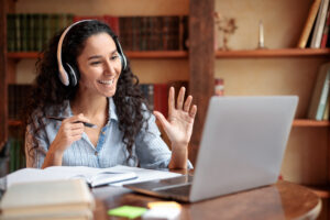Woman sitting at desk, using computer and waving to webcam
