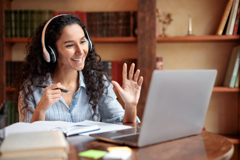 Woman sitting at desk, using computer and waving to webcam