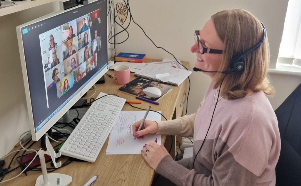 Sheridan Webb with a headset on, sitting at a desk with a computer running an online meeting (C) Sheridan Webb