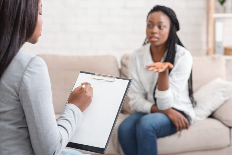 Psychologist taking notes during therapy session with her emotional female patient