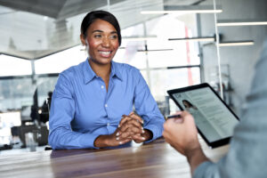 Happy African American young woman job seeker talking to professional male HR manager checking digital cv on tablet at interview meeting process. Company recruitment, human resources and hiring.