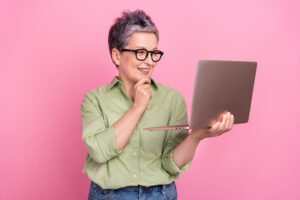 Portrait of cheerful minded corporate person hand touch chin use netbook watch video isolated on pink color background