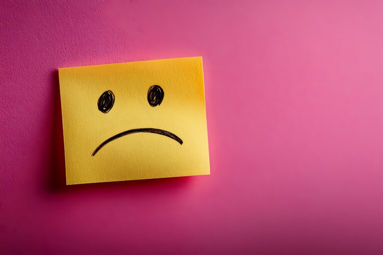 Yellow sticky note with hand drawn sad face on vibrant pink background showing negative emotion, depression or bad customer experience concept.