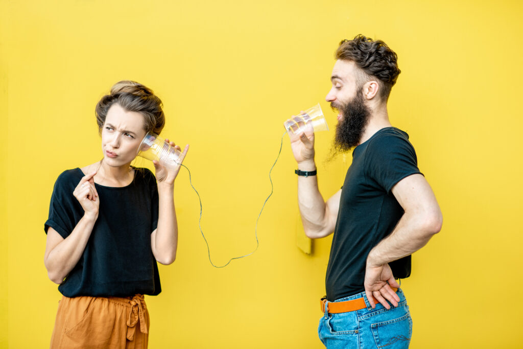Man and woman talking with string phone made of cups on the yellow background. Concept of communication