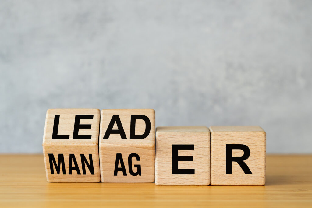 Manager vs leader symbol. Businessman arranged wooden cubes on the table to form the words manager to leader. Business concept. Beautiful gray background, copy space