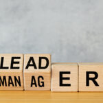 Manager vs leader symbol. Businessman arranged wooden cubes on the table to form the words manager to leader. Business concept. Beautiful gray background, copy space