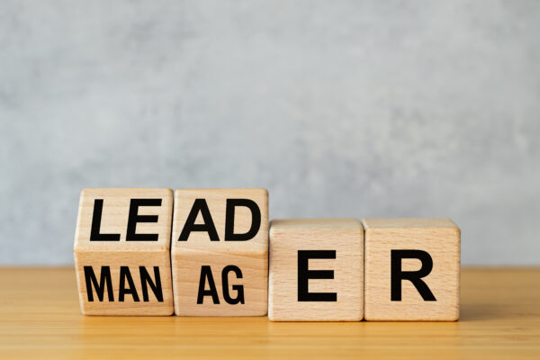 Manager vs leader symbol. Businessman arranged wooden cubes on the table to form the words manager to leader. Business concept. Beautiful gray background, copy space