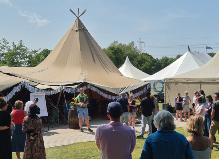 School of Facilitation Festival 2025 - a tent with people standing around in sunshine.