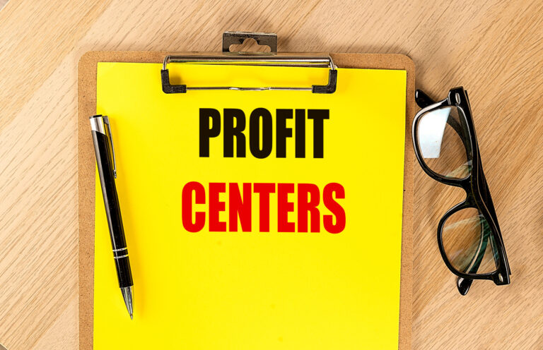 Clipboard with text profit centers on bright yellow paper next to pen and eyeglasses on wooden table