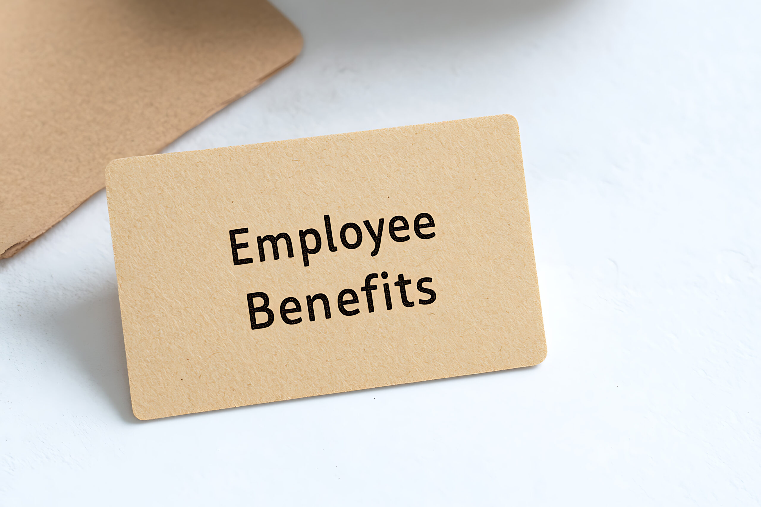 Paper card on a white surface showcasing text "Employee Benefits". Minimalist composition highlighting employment compensation and advantages.