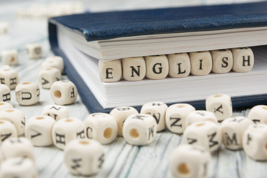 Word english made with block wood letters next to a pile of other letter over  wooden table