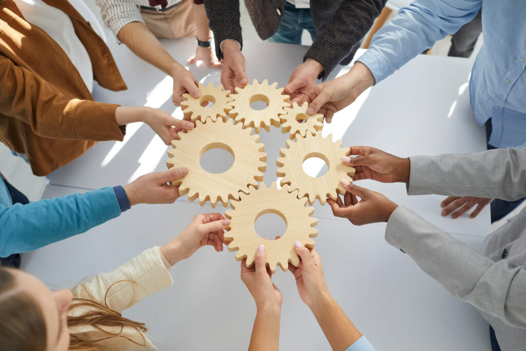 Hands close-up of group multiethnic business people connect wooden gears in the center. Arial view. Success cooperation teamwork concept, connection technology concept