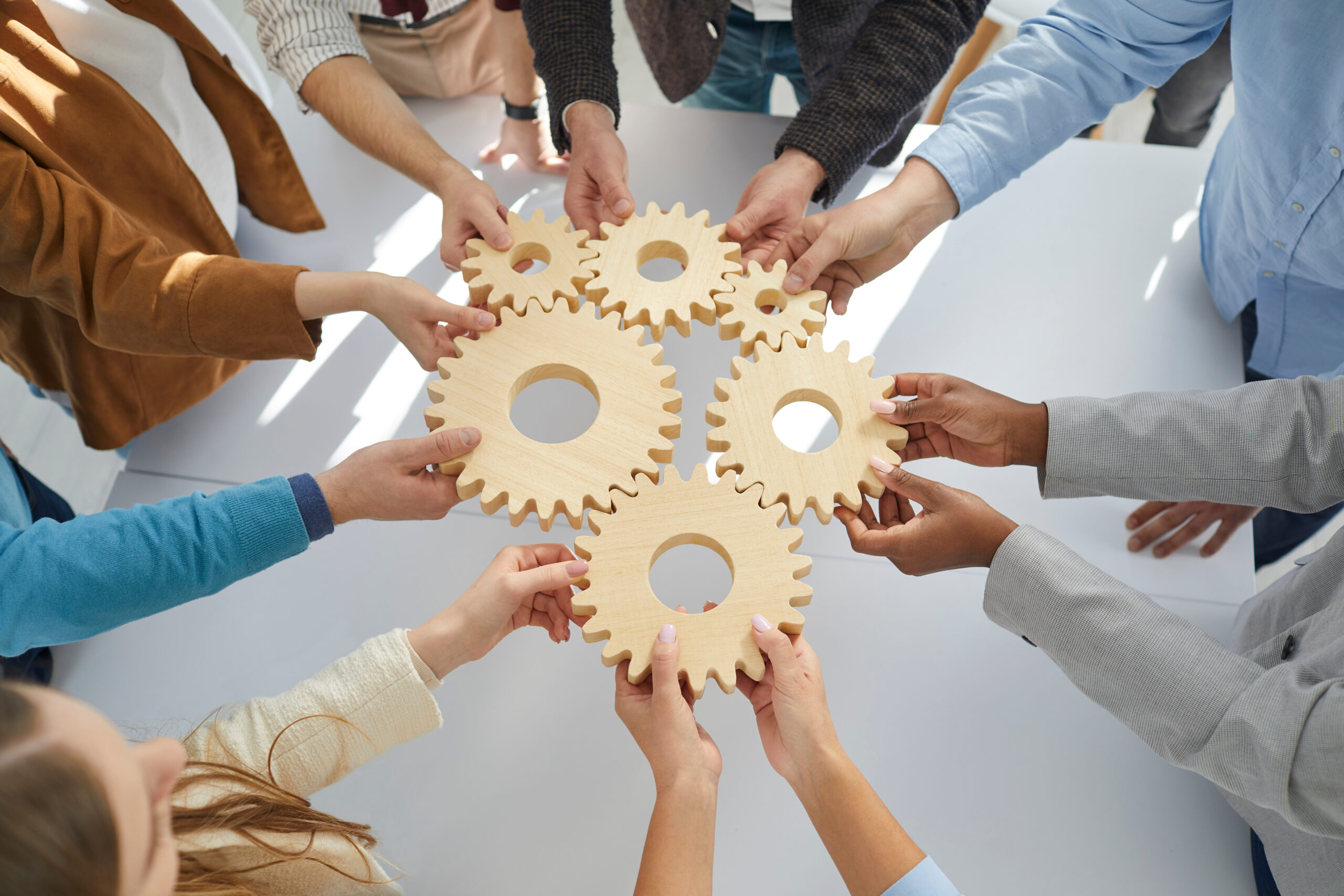 Hands close-up of group multiethnic business people connect wooden gears in the center. Arial view. Success cooperation teamwork concept, connection technology concept