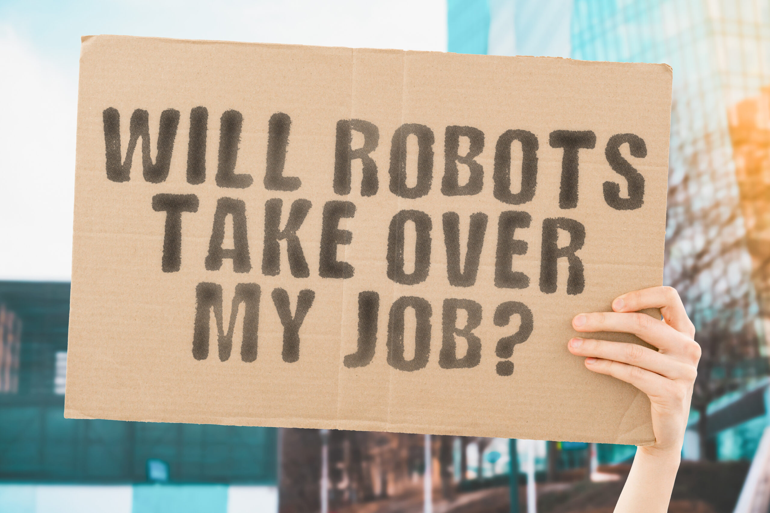 The question " Will robots take over my job? " on a banner in men's hand with blurred background. Automation. Technology. Worker. AI. Artificial intelligence. Future. Profession. Occupation
