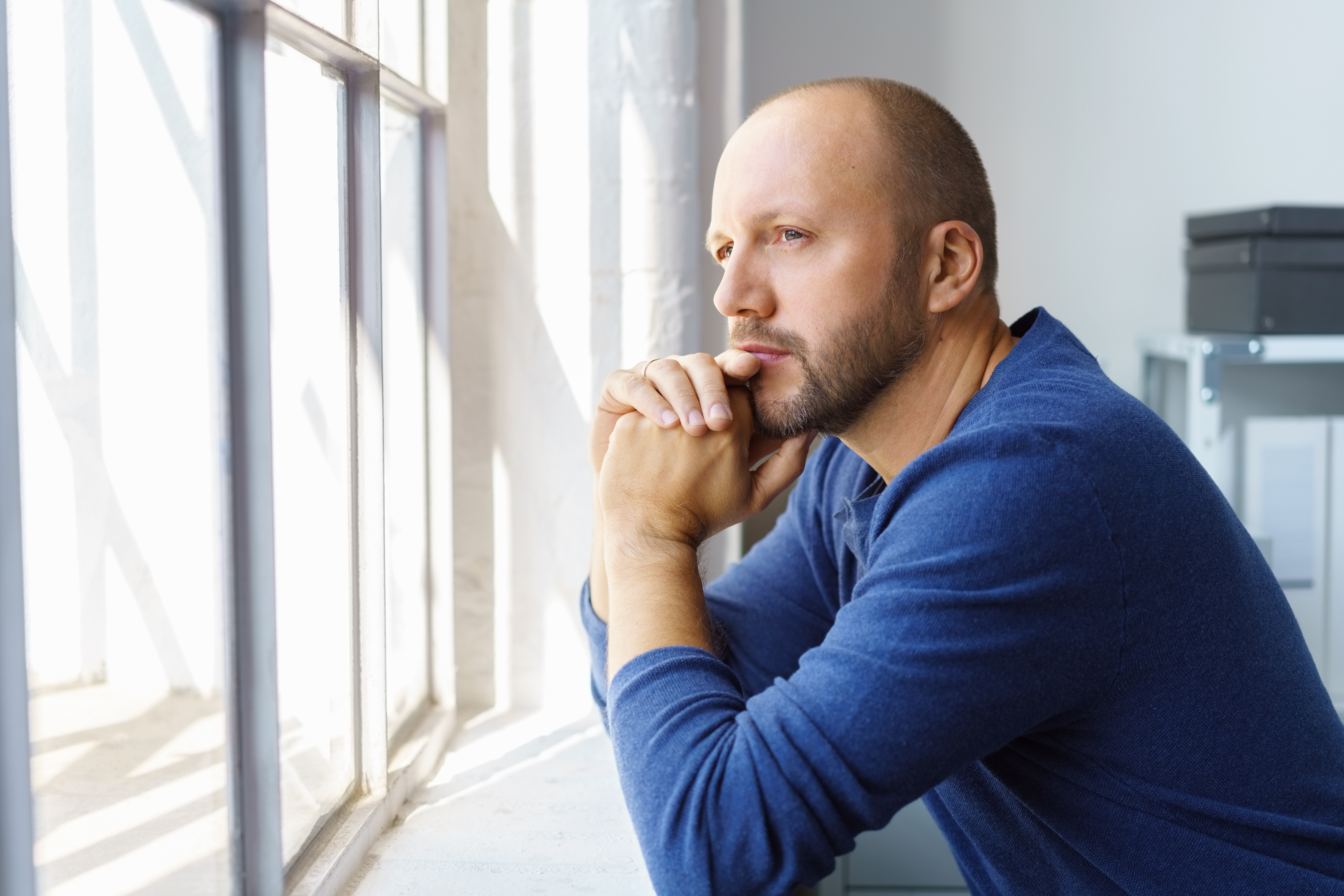 White 35-40 year old man pausing and thinking, looking out of a window, reflecting on work.