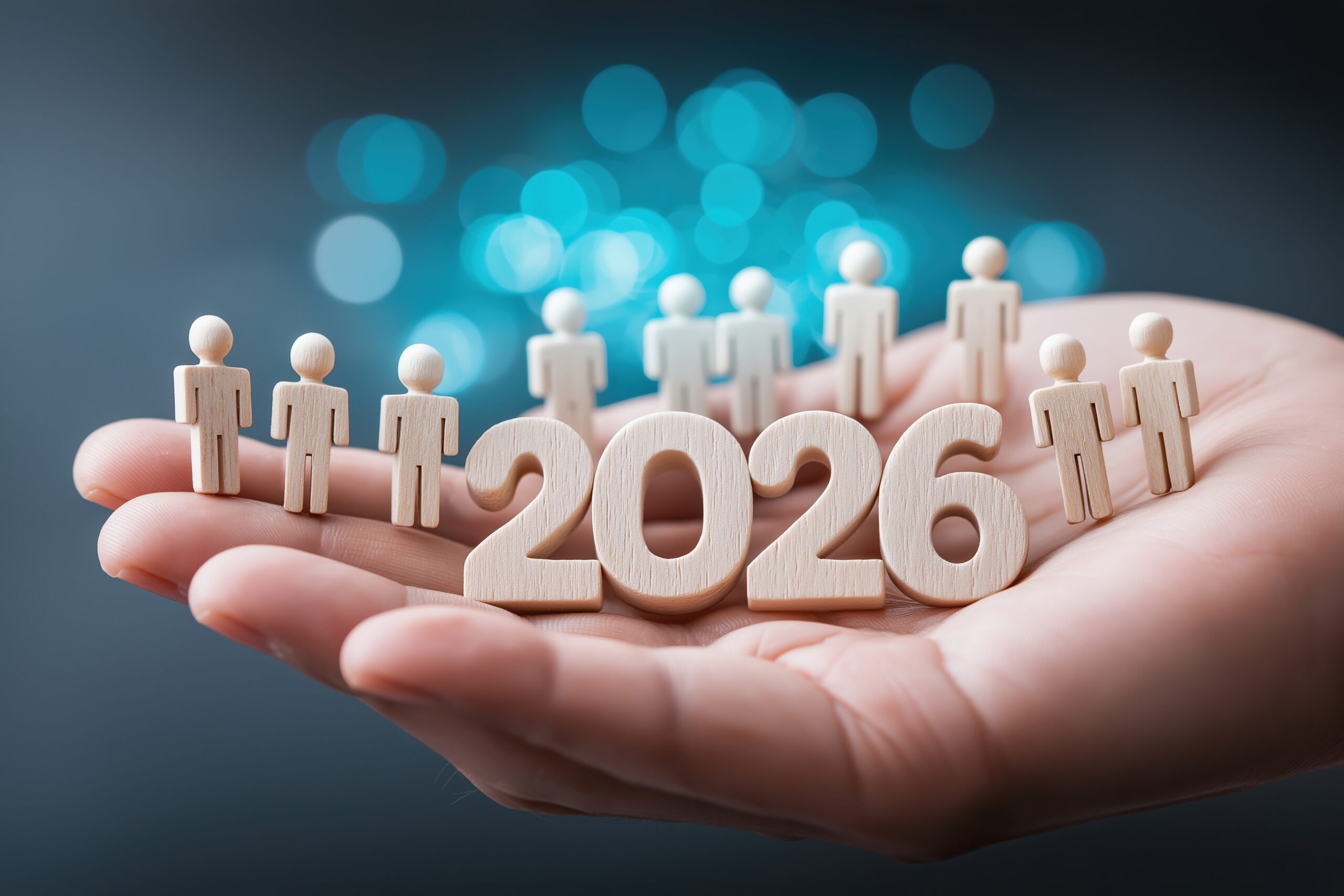Open hand holds wooden people around 2026 digits against shimmering blue background.