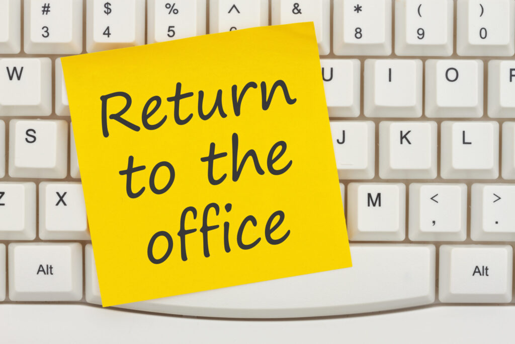 Return to the office message on a yellow sticky note on a gray computer keyboard