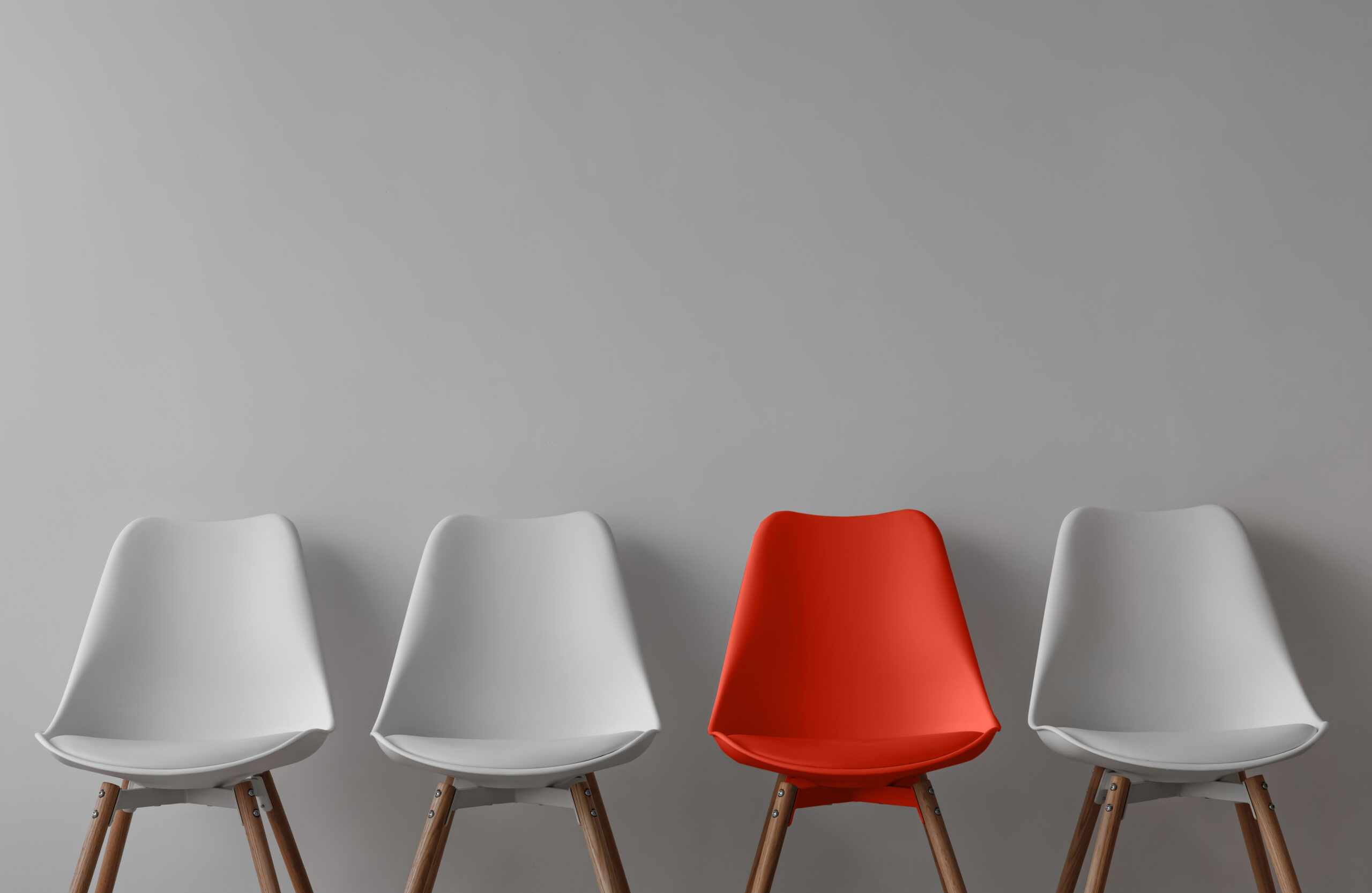 Three white chairs and red on gray wall background in office or room. Row of stools with one of different colour. Job opportunity, recruitment, business, leadership and hiring concept, copy space