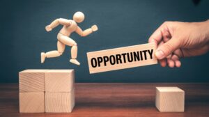 Wooden mannequin jumping across a gap while a human hand provides a bridge labeled Opportunity on a dark background