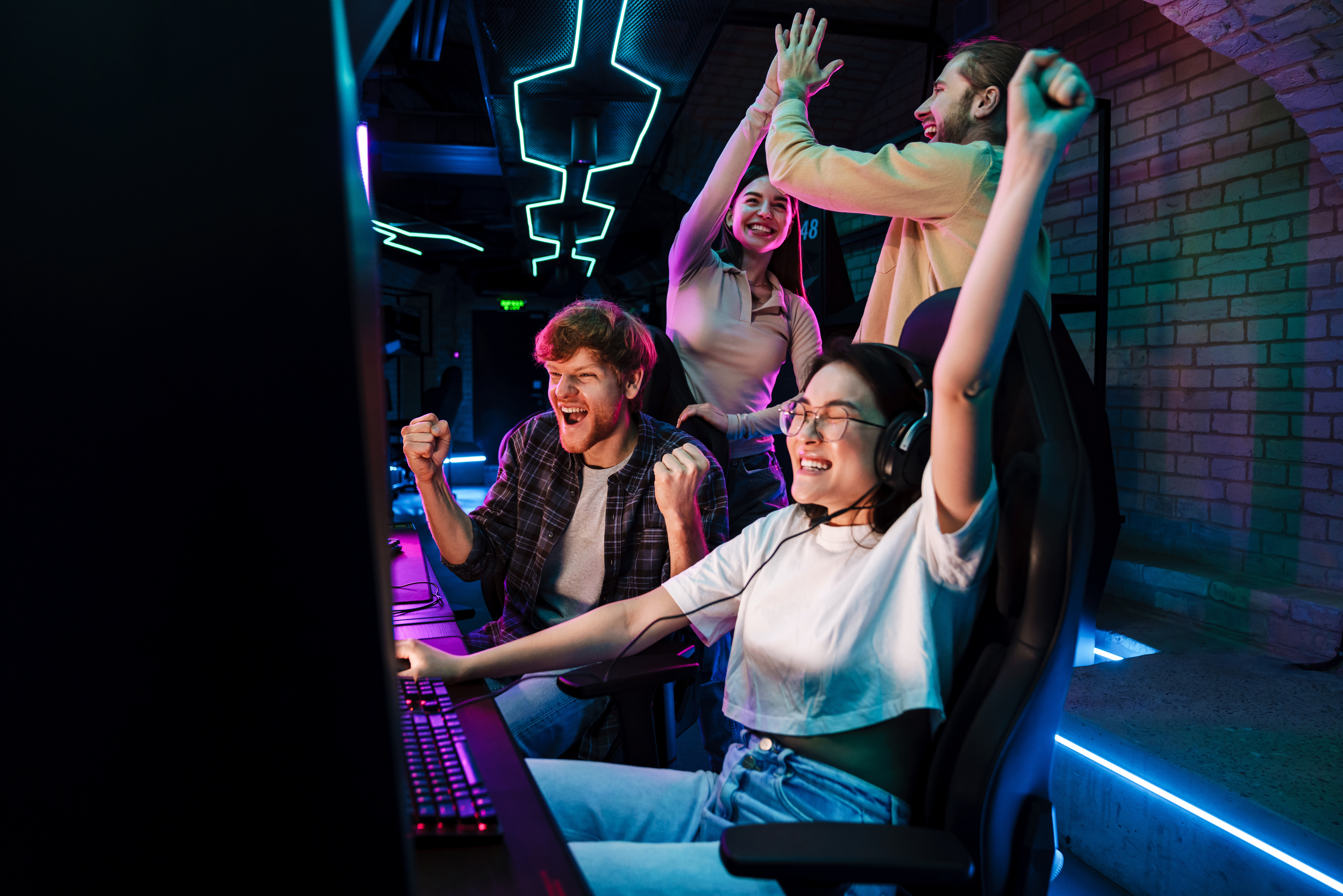 Group of friends celebrating victory of asian girl in video game while standing next to her in cybersport club
