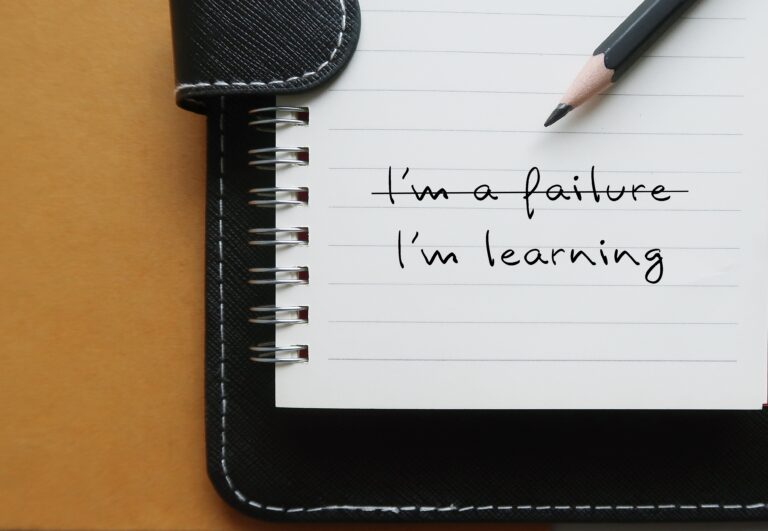 Notebook with text I'M A FAILURE crossed off to LEARNING, replace negative self-talk with positive thoughts, learn to build self-acceptance and embrace failure as part of growth and learning