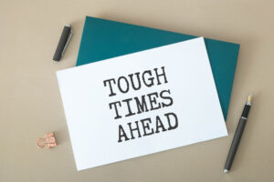 Tough Times Ahead text in lightbox with alarm clock on pastel background.