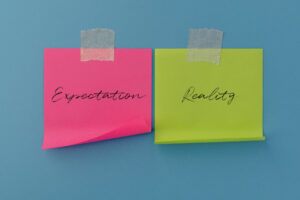 Two sticky notes with handwritten Expectation and Reality. Business results, comparison, performance evaluation, and strategic planning concept.