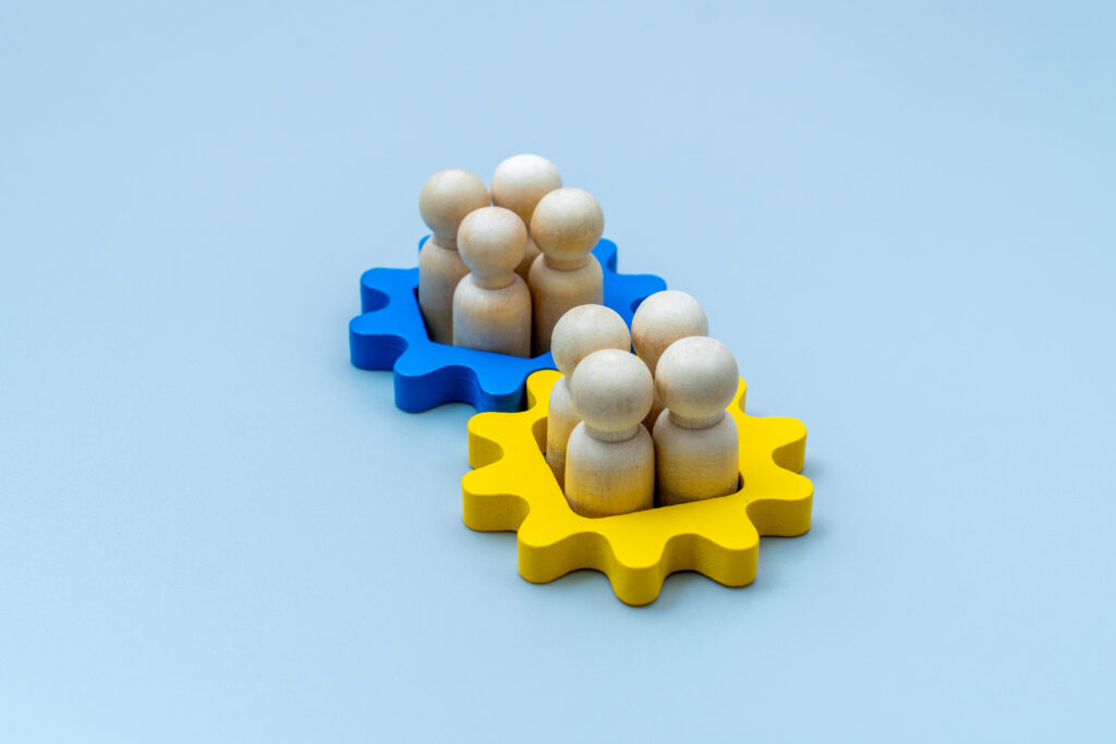 Wooden human figures inside blue and yellow gear shapes. Mergers and acquisitions, teamwork, integration, and corporate collaboration concepts.