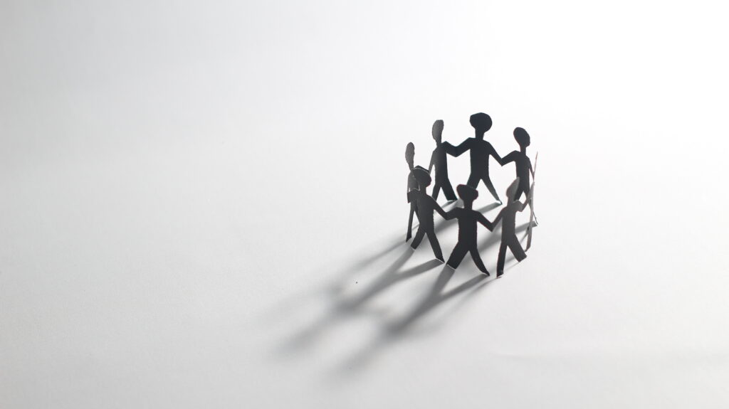Paper chain people holding hands in a circle on a white background, symbolizing unity, teamwork, and community connection. Black and white minimalist concept.