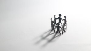 Paper chain people holding hands in a circle on a white background, symbolizing unity, teamwork, and community connection. Black and white minimalist concept.