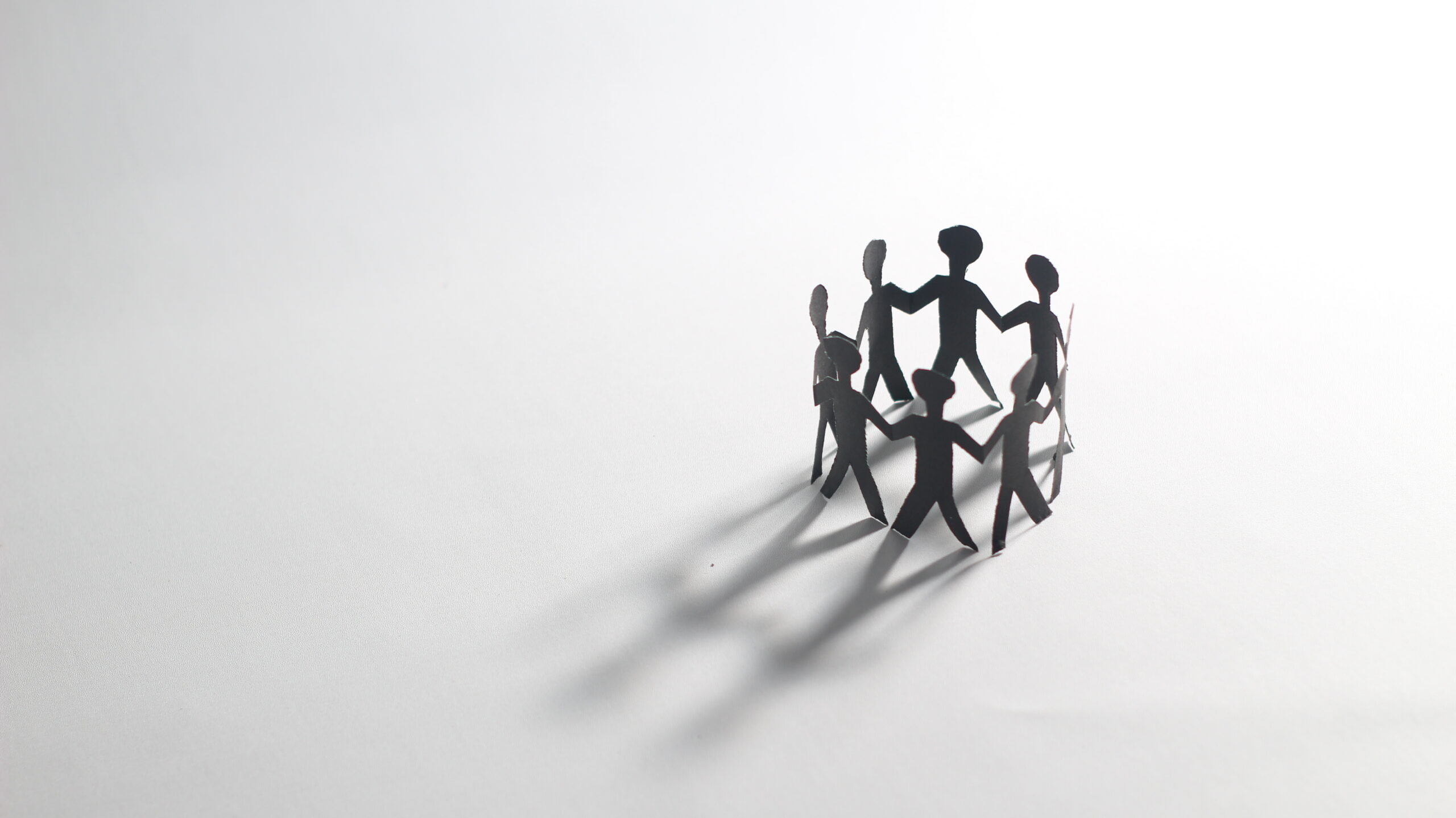 Paper chain people holding hands in a circle on a white background, symbolizing unity, teamwork, and community connection. Black and white minimalist concept.