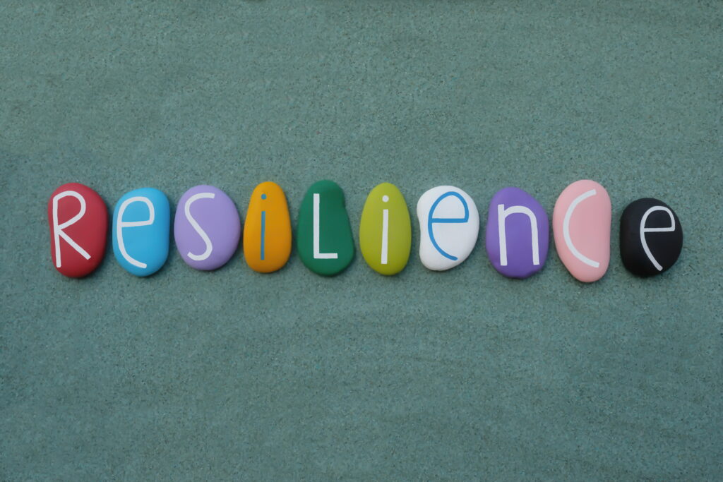 Resilience, the ability to be happy or successful again after something difficult or bad has happened. Creative handmade multicolored stone letters of resilience text over green sand