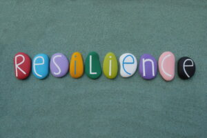 Resilience, the ability to be happy or successful again after something difficult or bad has happened. Creative handmade multicolored stone letters of resilience text over green sand