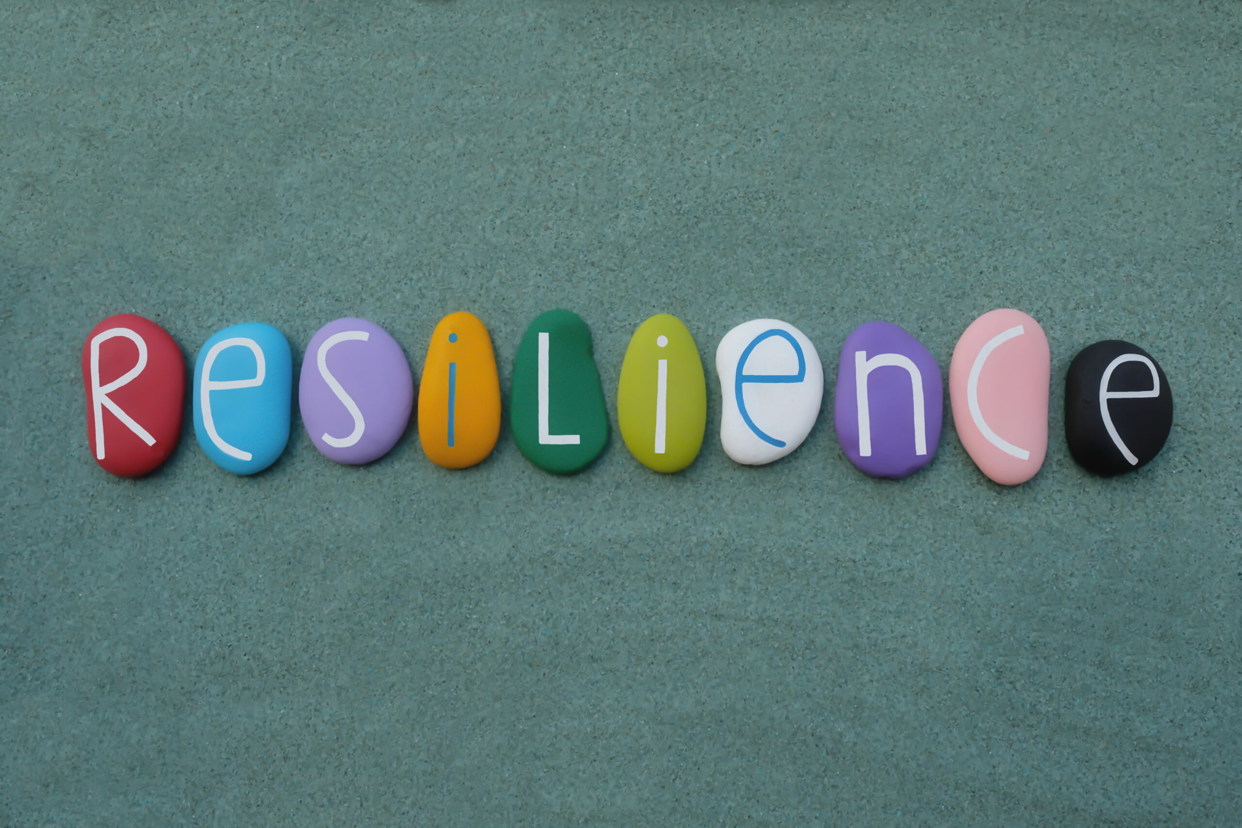 Resilience, the ability to be happy or successful again after something difficult or bad has happened. Creative handmade multicolored stone letters of resilience text over green sand