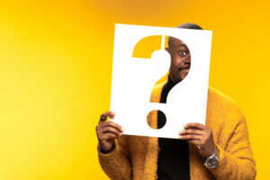 A person holding a large white question mark over their face against a vibrant yellow background illustrating curiosity and mystery