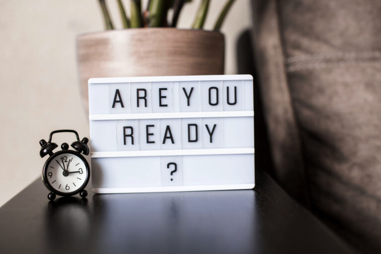A room flower, standing on the back of a sofa, a clock and a light box with words are you ready.