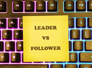 A yellow sticky note displays Leader VS Follower in bold text on a modern computer keyboard with colorful backlighting